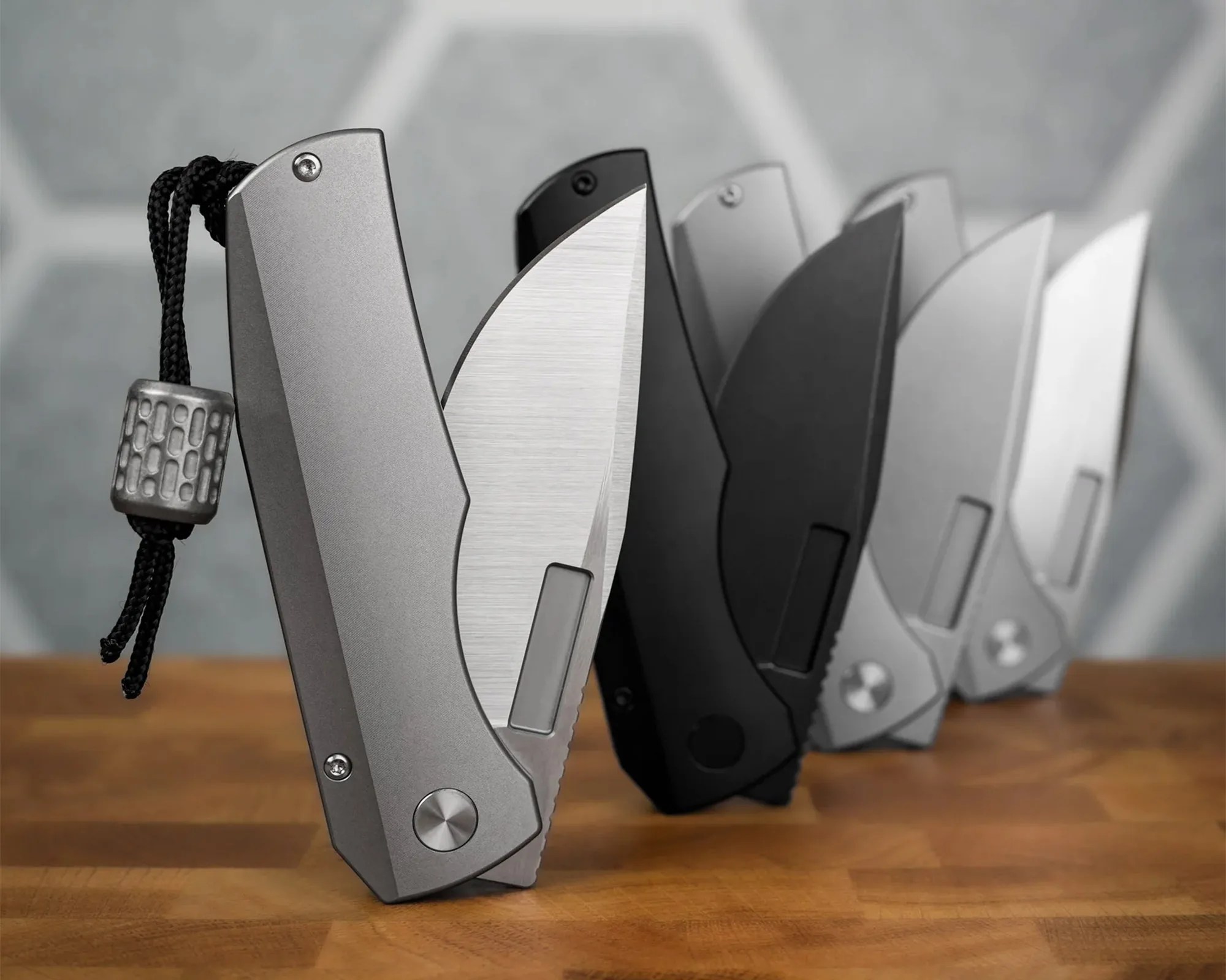 Five folding knives with partially open blades in various finishes, standing on a wooden surface.