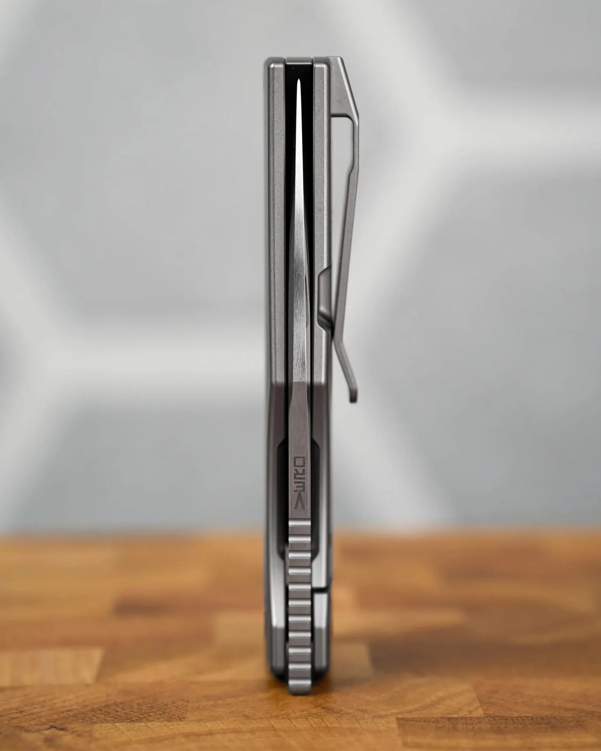 Close-up of a closed folding knife with a metal clip on a wooden surface.