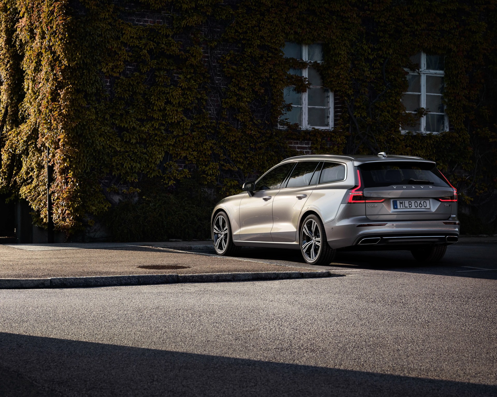 Silver Volvo V60 station wagon parked on a street beside a building covered in ivy.