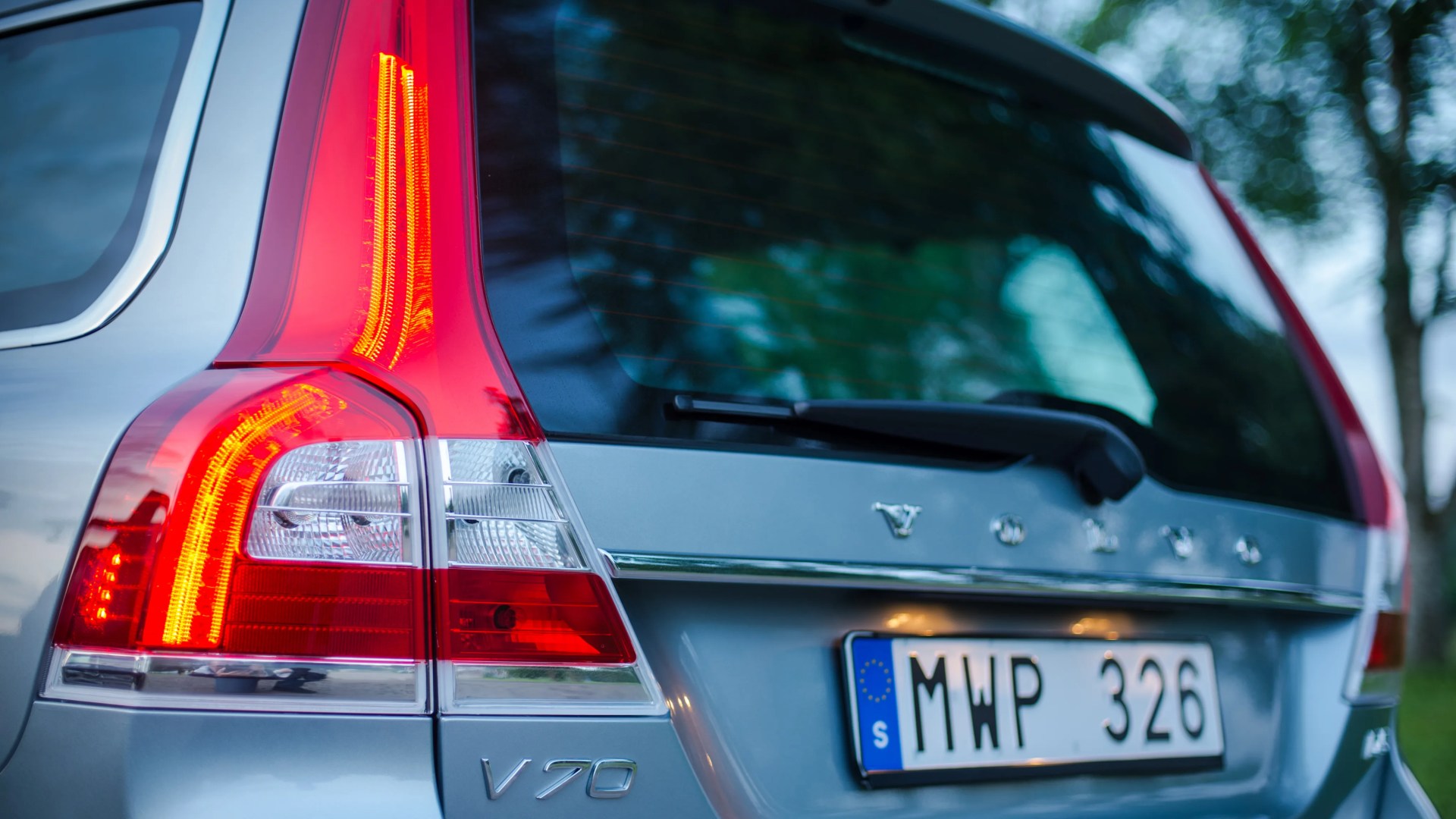 Rear view of a silver Volvo V70 with illuminated taillight and European license plate.