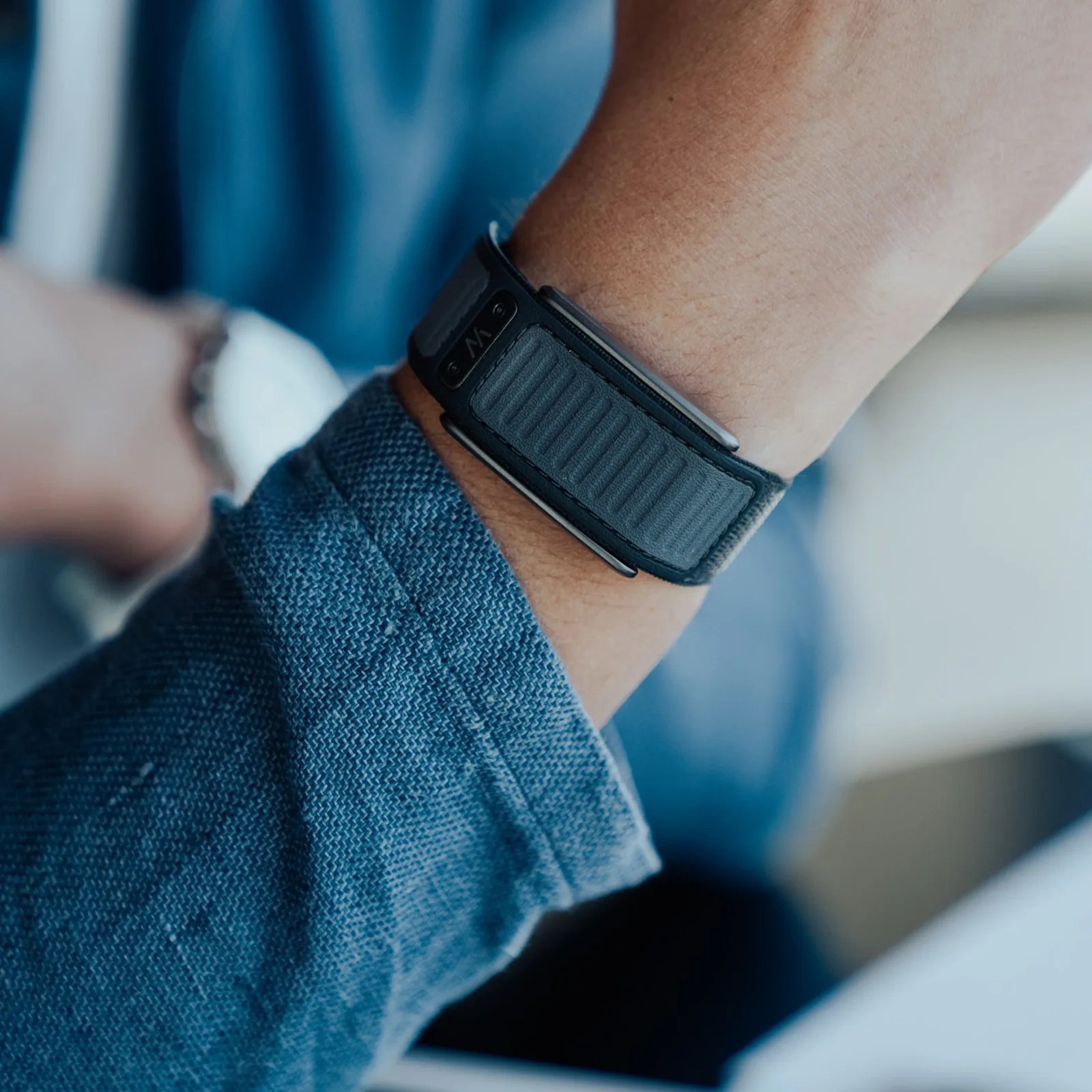 Black and gray fabric watch strap fastened on a wrist with a blue denim sleeve.