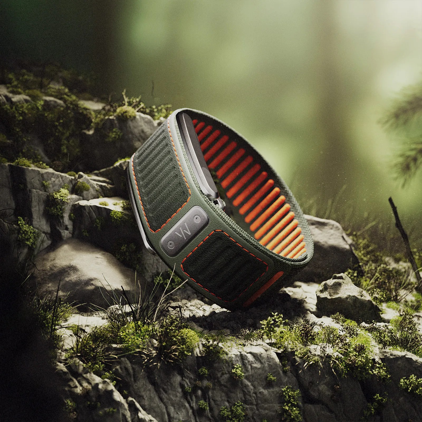 Green and orange textured wristband with a black device attached, resting on mossy rocks.