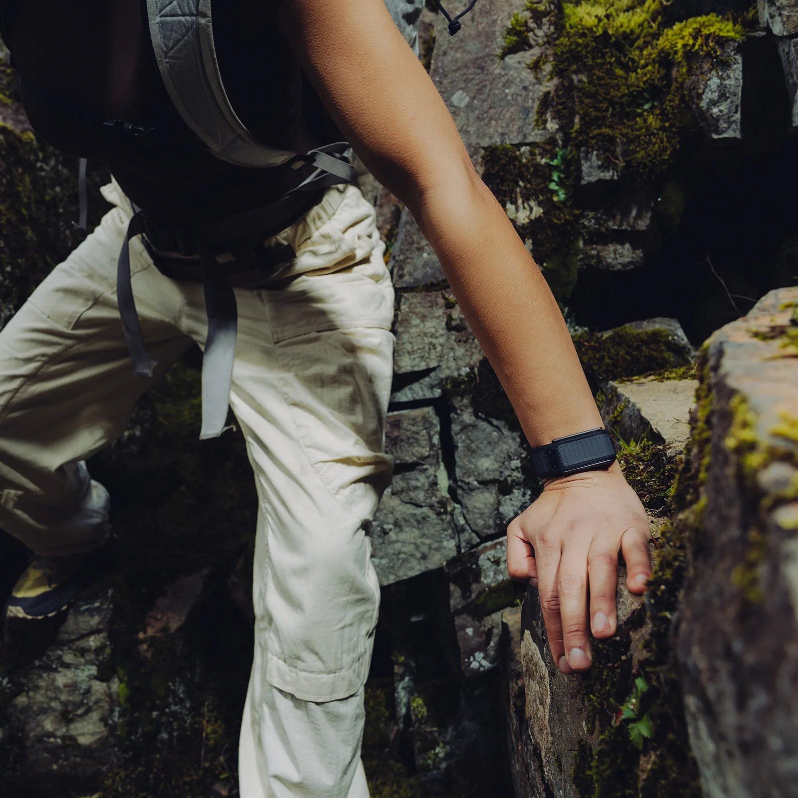 Person wearing beige pants and a black smartwatch climbing moss-covered stone steps.