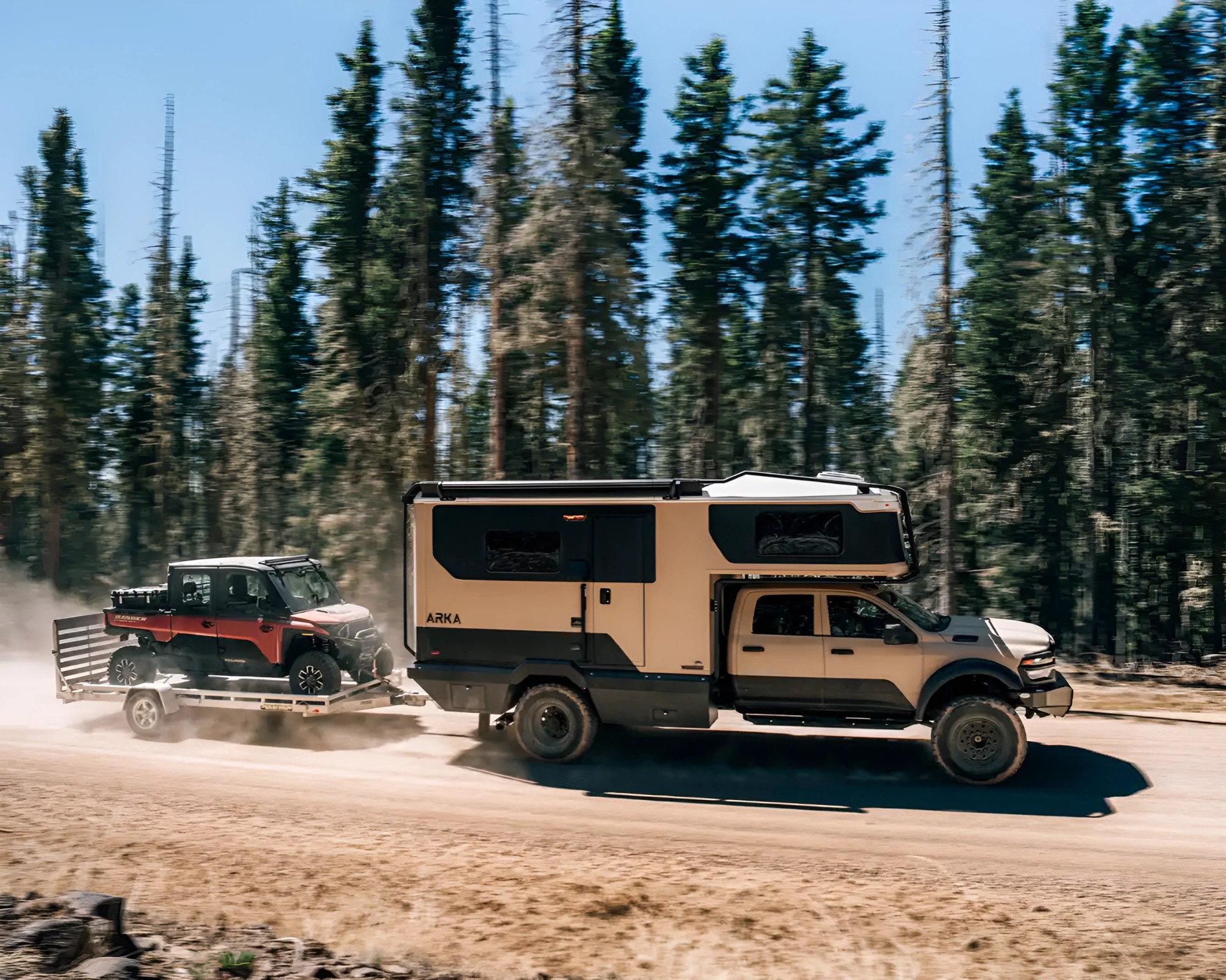 Beige and black ARKA camper truck towing a red off-road vehicle on a trailer on a dirt road with pine trees in the background.