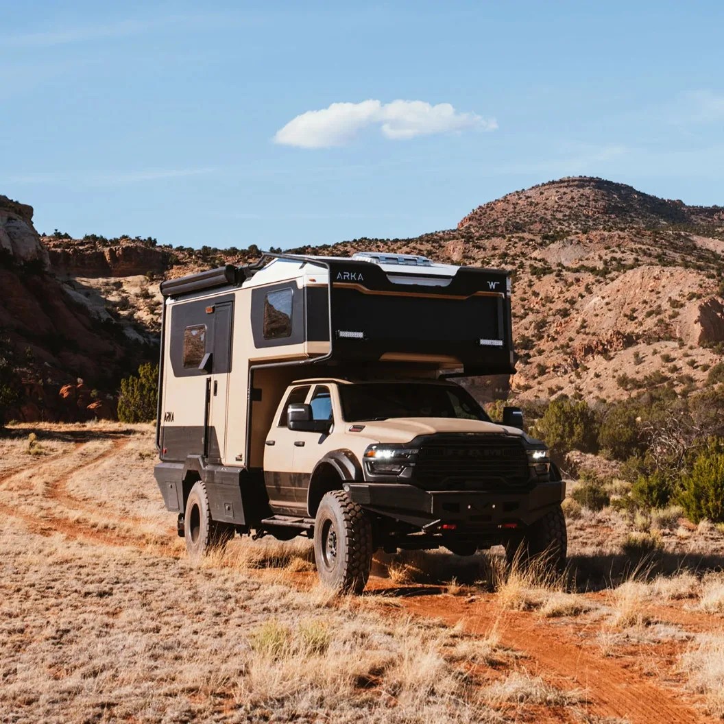 Beige and black off-road camper truck parked on a dirt trail in a rocky desert landscape.