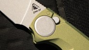 Close-up of a knife blade marked "CPM-3V" with a green textured handle and circular metal pivot.