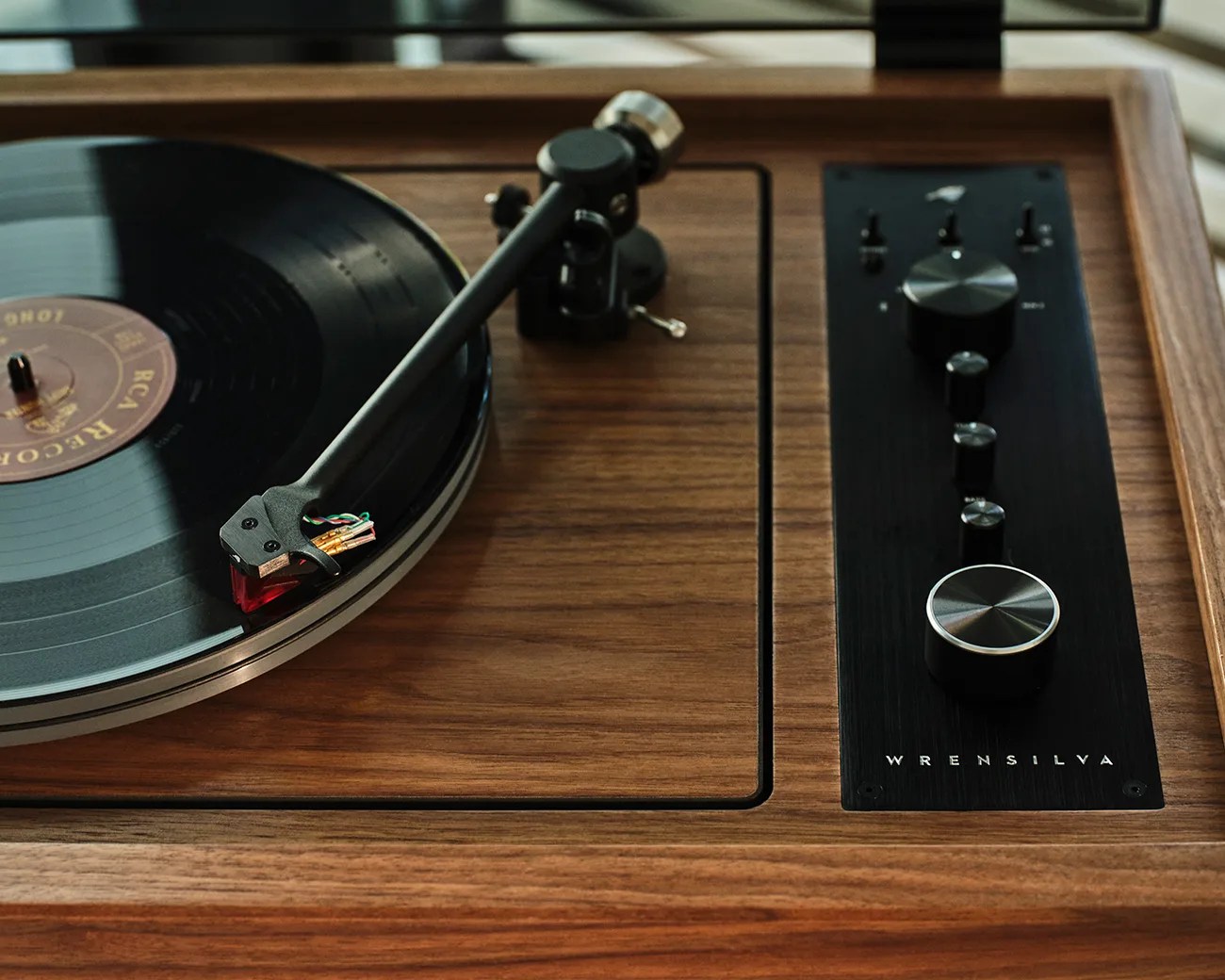 Turntable with black tonearm and vinyl record on a wooden base with black control panel labeled "WRENSILVA.