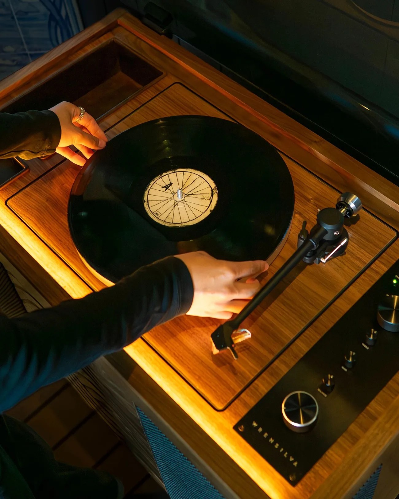 Hands placing a black vinyl record on a wooden Vientilva turntable with a tonearm and control knobs.