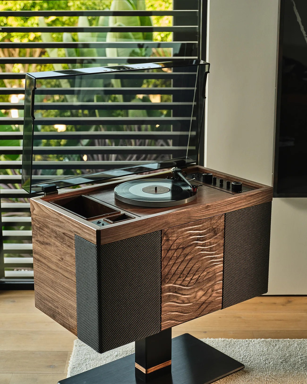 Wooden vintage-style record player with black mesh speakers and a transparent dust cover, standing on a black pedestal.