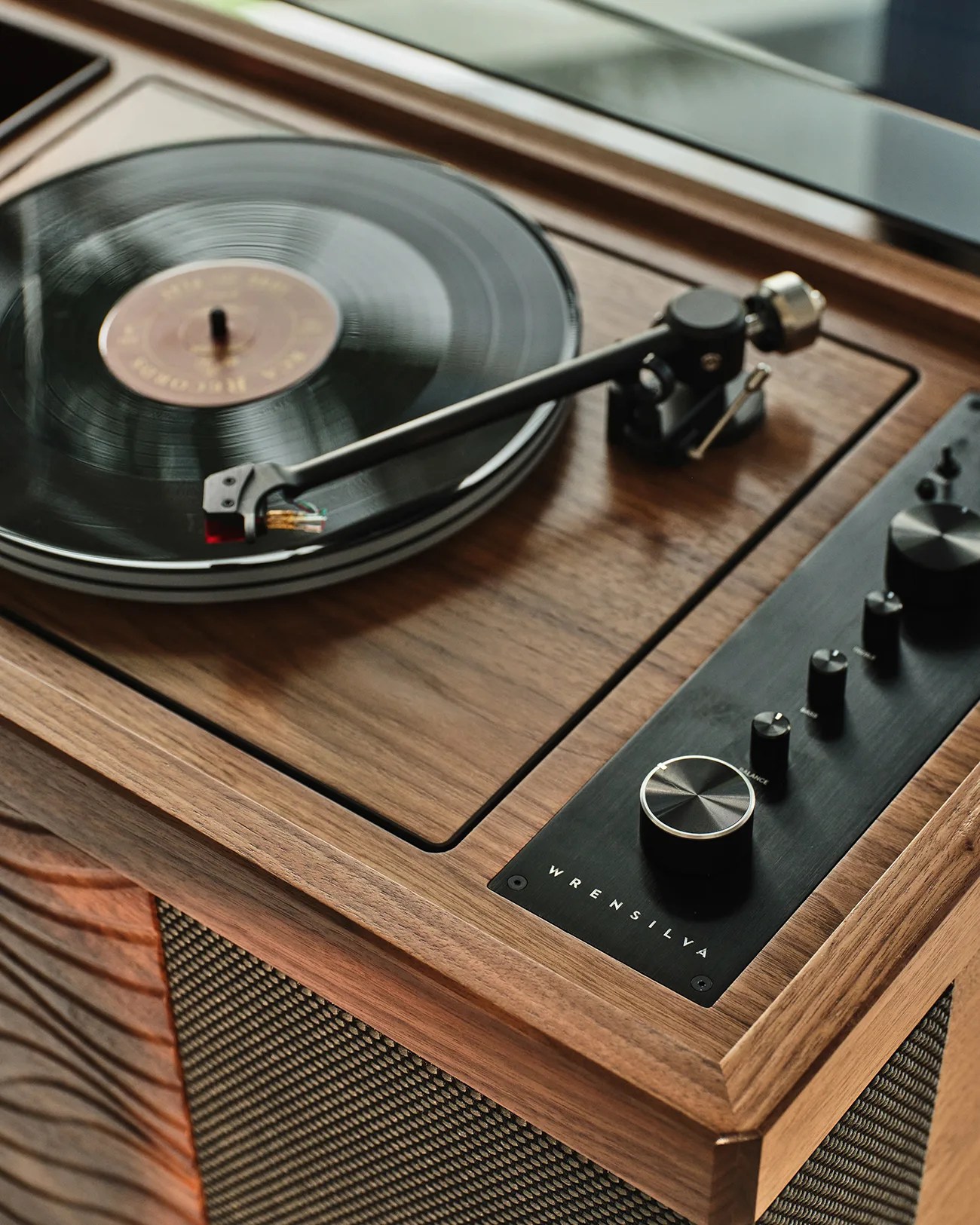 Wooden turntable with black vinyl record spinning and control knobs labeled "Wrensilva" on the side panel.