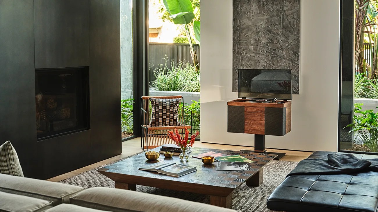 Modern living room with a black fireplace, wooden coffee table with decor, rattan chair, and a wooden record player stand.