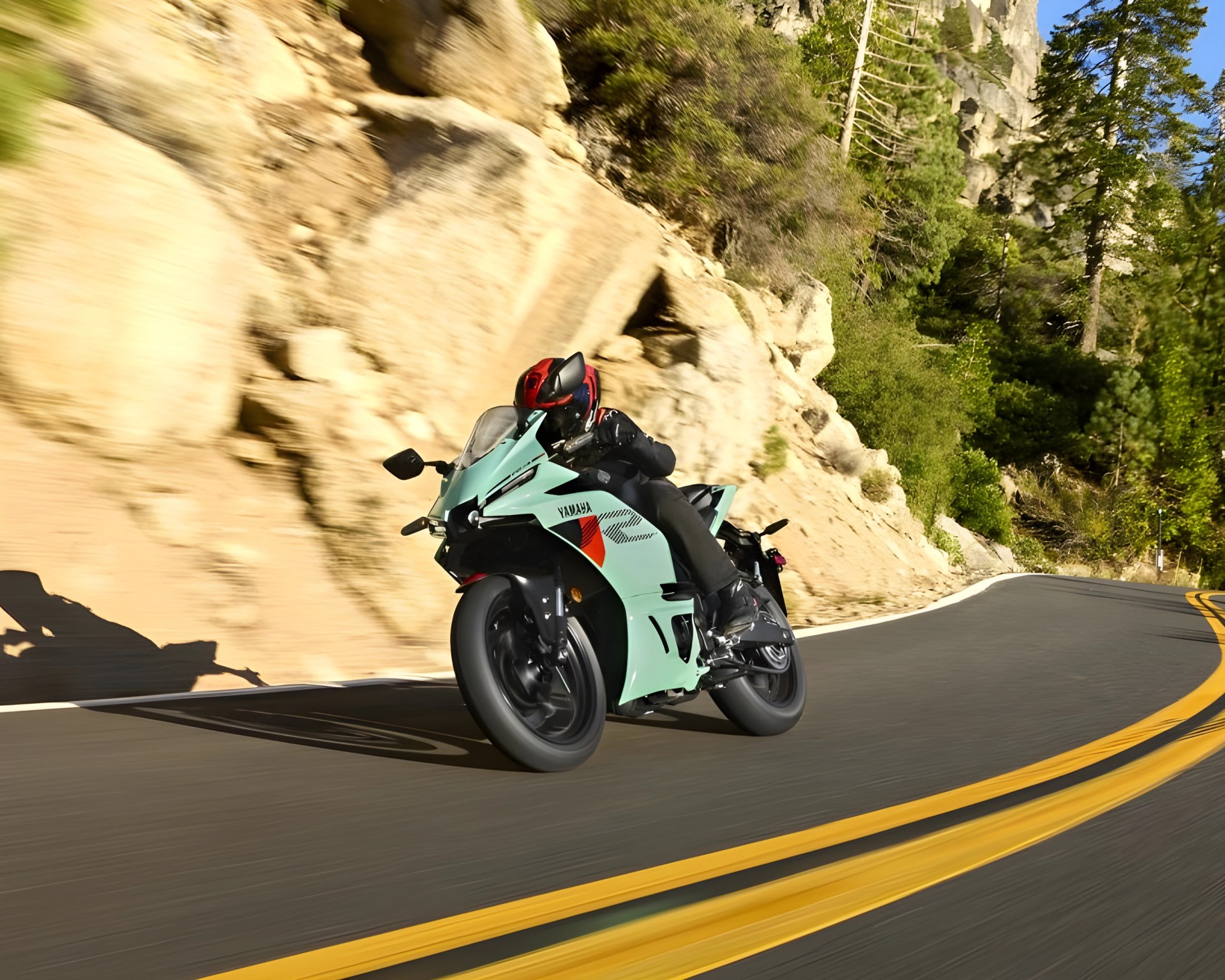 Light blue Yamaha sport motorcycle with red and black accents leaning into a curve on a mountain road.
