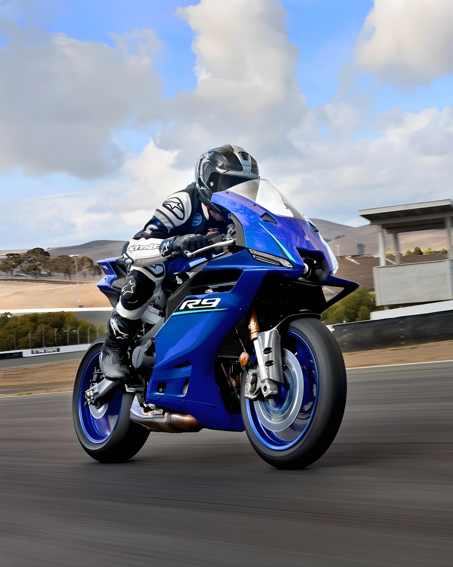 Blue Yamaha R9 sport motorcycle with rider in black and white racing gear on a racetrack.