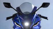 Front view of a blue sport motorcycle with black side mirrors, clear windshield, and illuminated headlights.