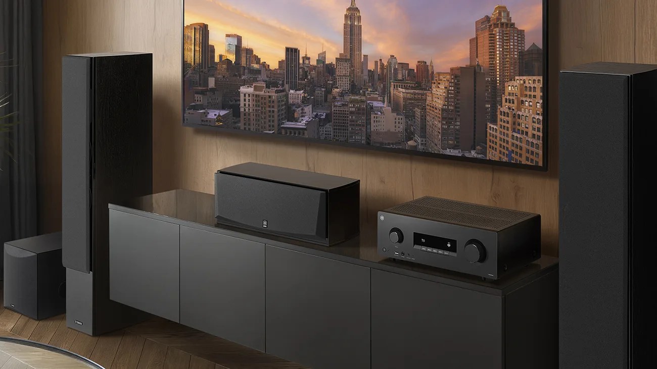 Black home audio system with tall speakers, center speaker, and receiver on a black cabinet under a wall-mounted TV.