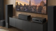 Black home audio system with tall speakers, center speaker, and receiver on a black cabinet under a wall-mounted TV.