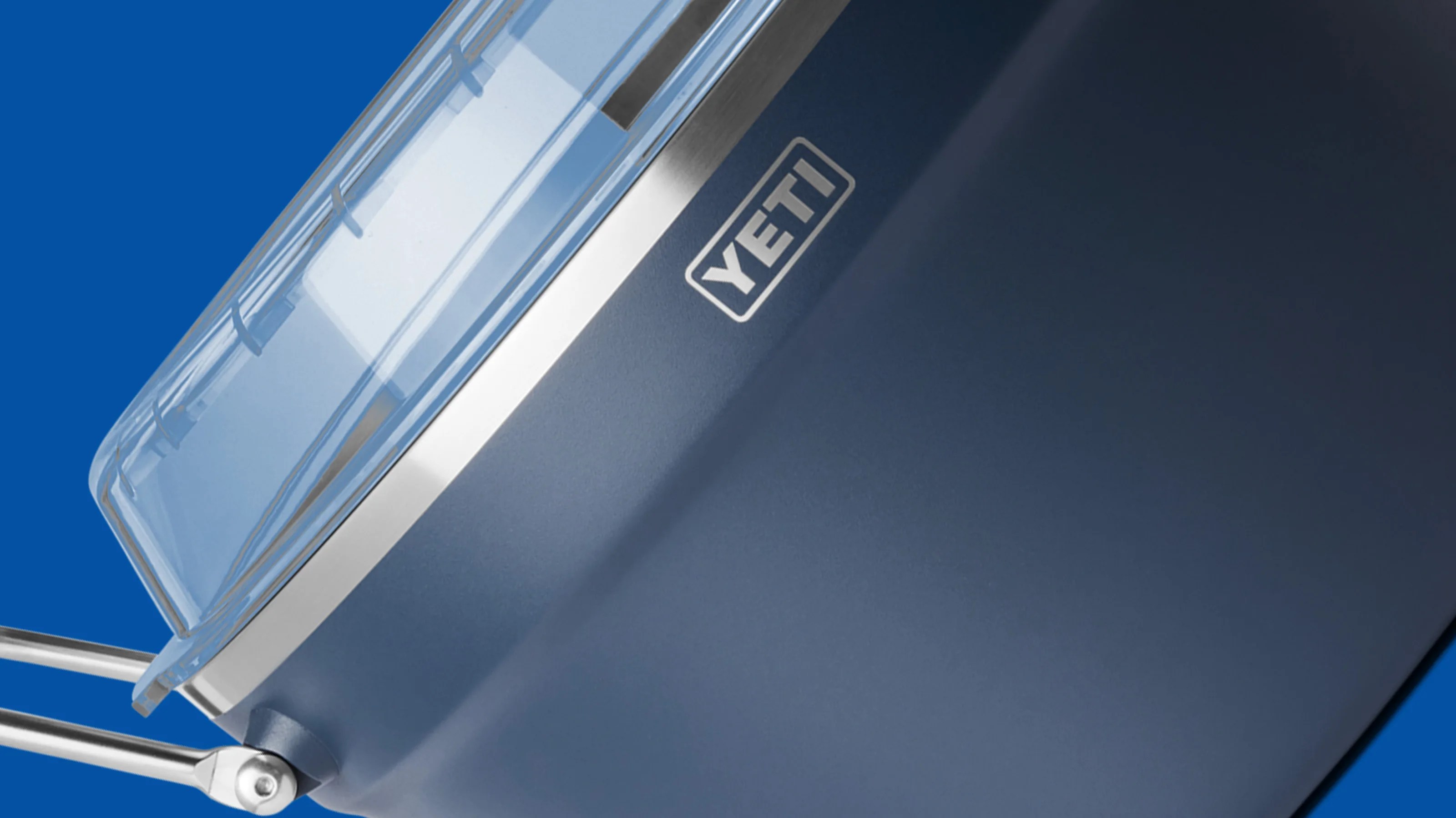 Close-up of a blue YETI cooler with a clear lid and silver metal handle against a blue background.