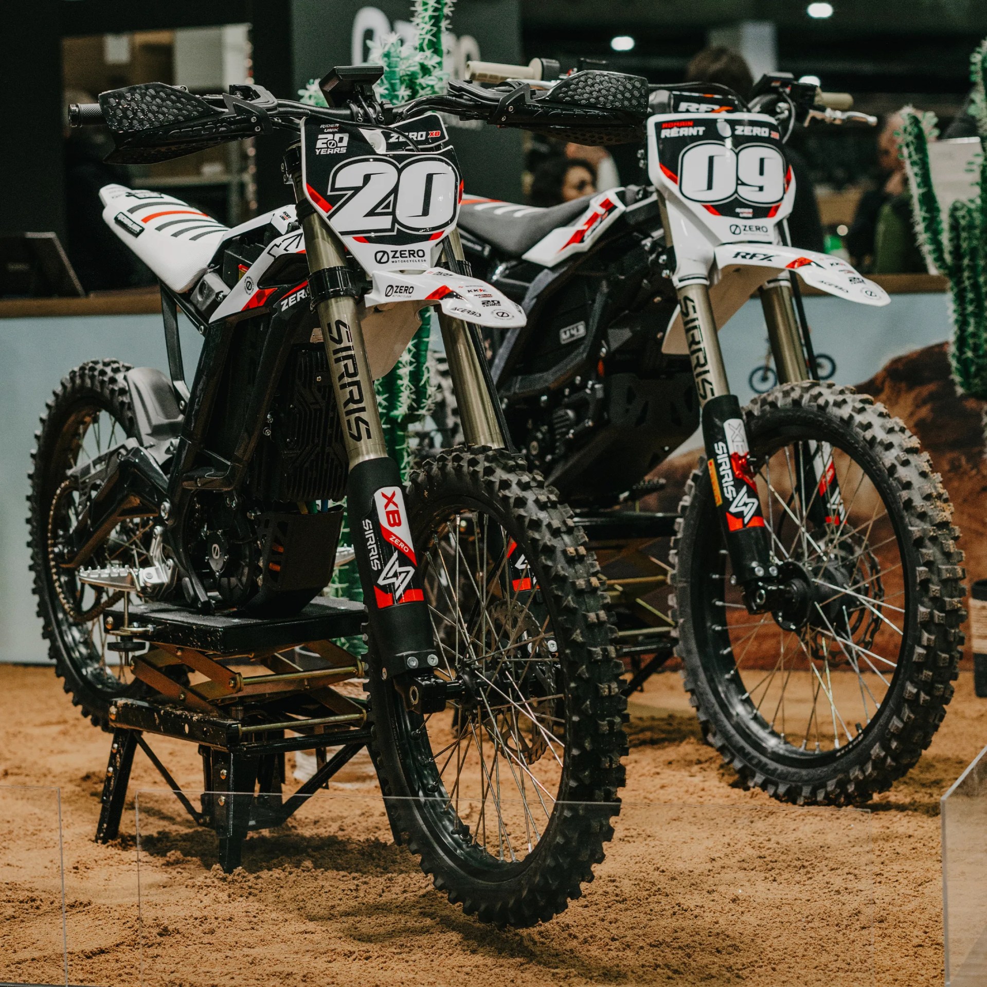 Two white and black dirt bikes with red accents and large knobby tires on a sandy surface.
