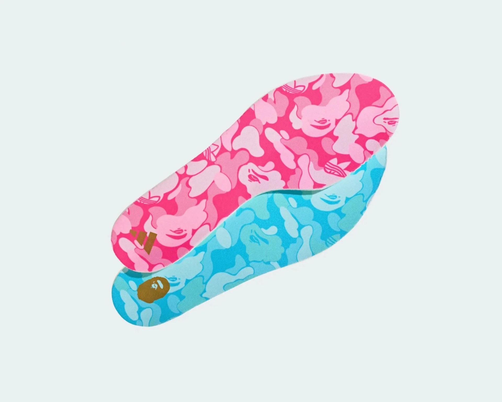 Pair of shoe insoles with pink and blue camouflage patterns featuring abstract faces and logos.
