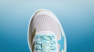 White and light blue athletic shoe with mesh upper and light blue laces on a blue gradient background.