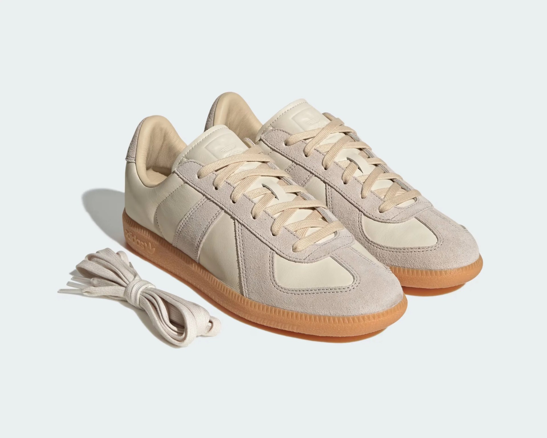 Pair of beige Adidas sneakers with suede accents and gum soles, accompanied by extra beige laces.