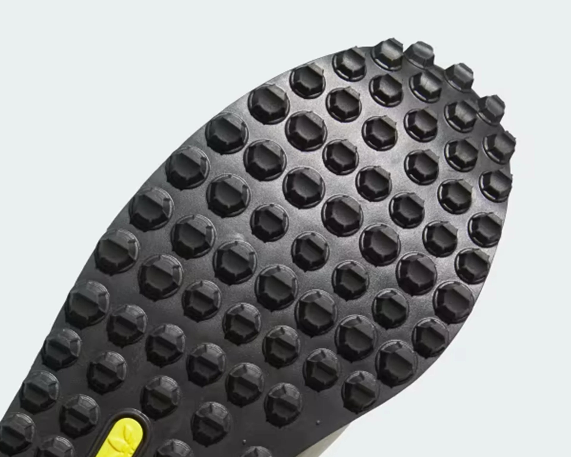 Black shoe sole with hexagonal rubber studs and a small yellow oval logo near the bottom.