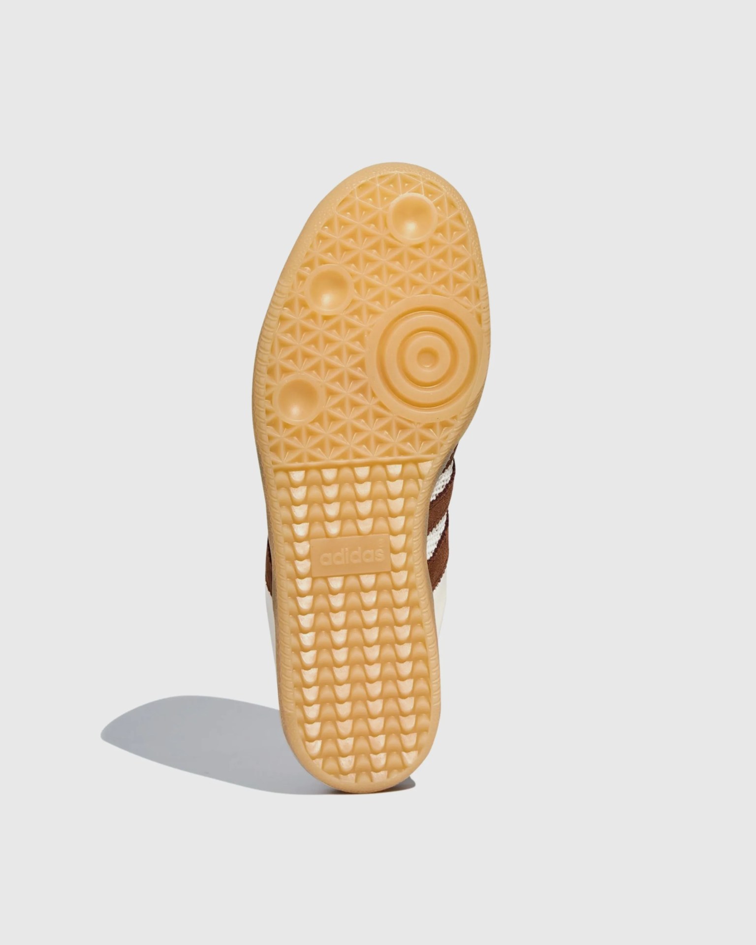 Gum rubber sole of a brown Adidas shoe with textured grip and Adidas logo.