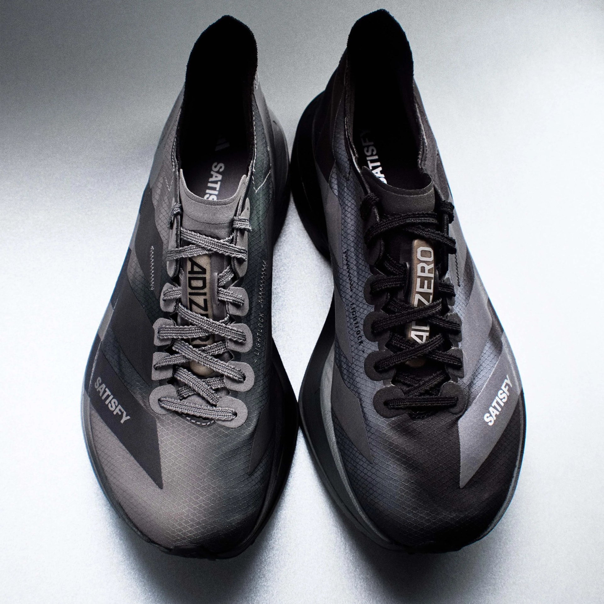 Pair of gray and black running shoes with "SATISFY" branding on the sides and laces, viewed from above.