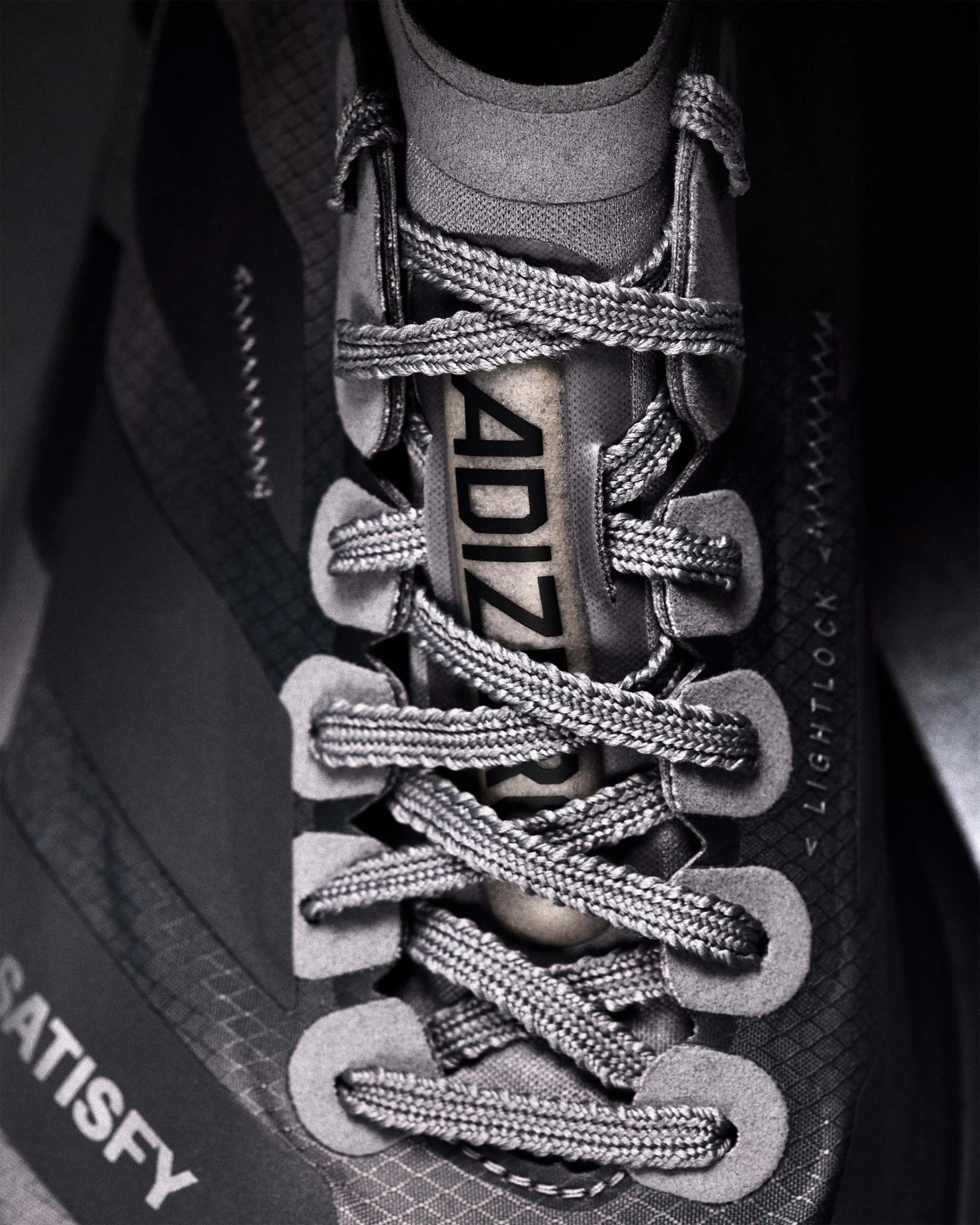 Close-up of gray braided shoelaces on a gray sneaker with "ADIZERO" and "SATISFY" text visible.