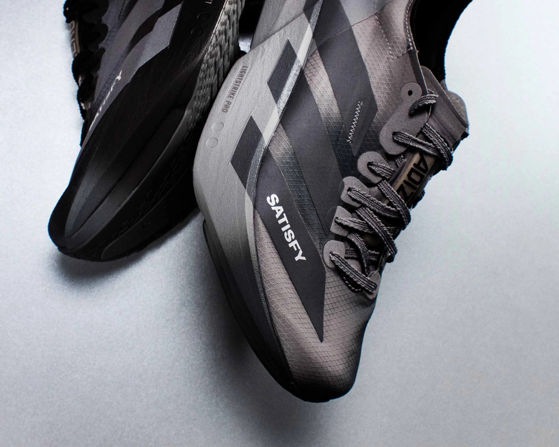Pair of gray Adidas running shoes with black stripes and "SATISFY" text on the side.