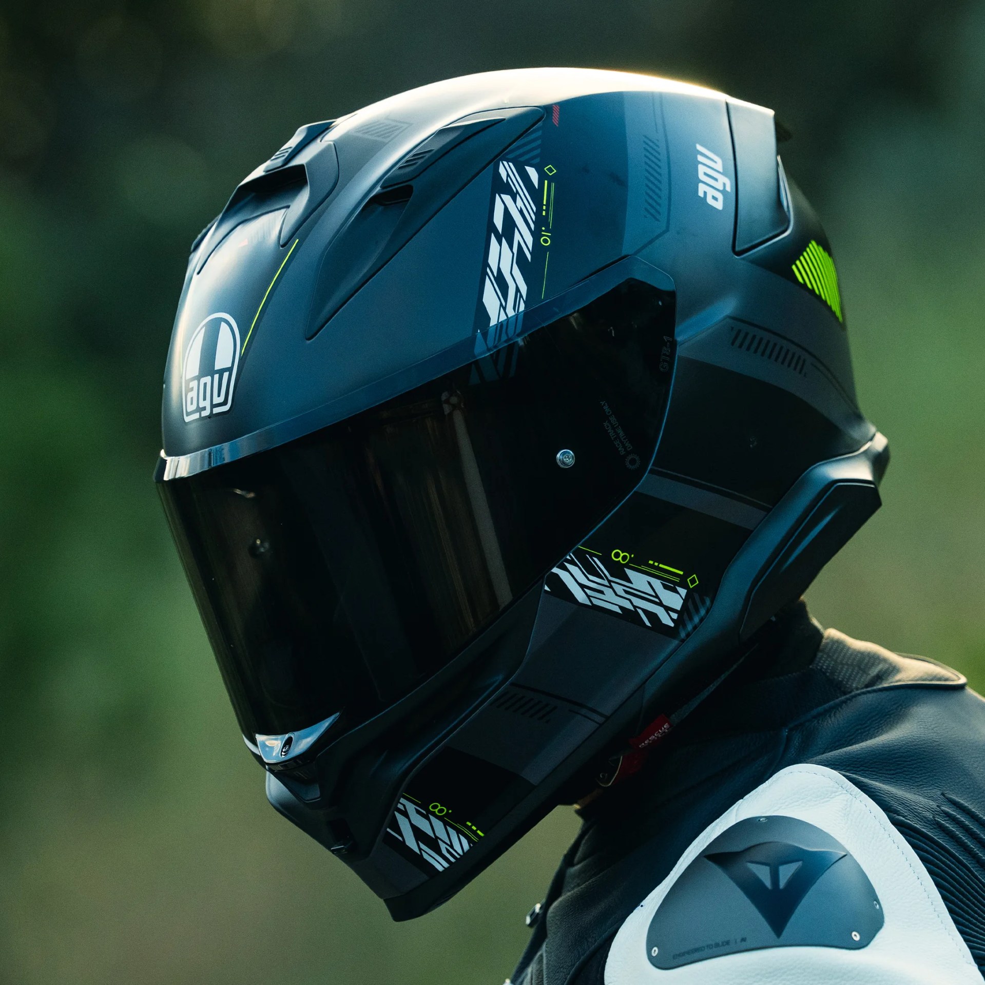 Black AGV motorcycle helmet with neon green and white graphics worn with a black and white leather jacket.