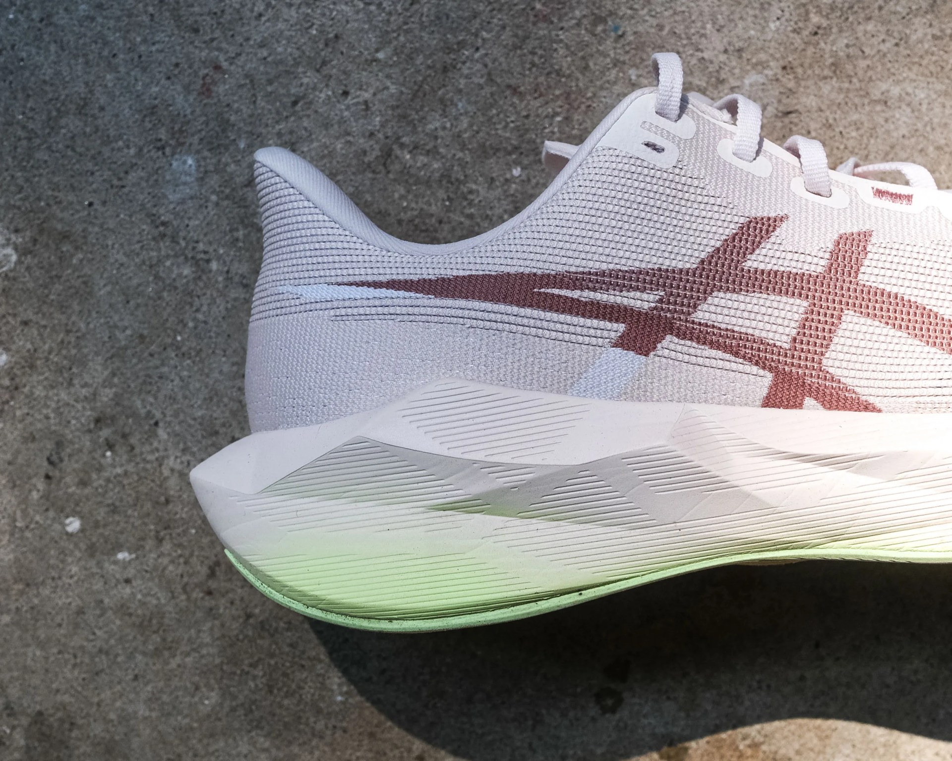 Close-up of a white athletic shoe with a brown Asics logo and a textured sole on a concrete surface.
