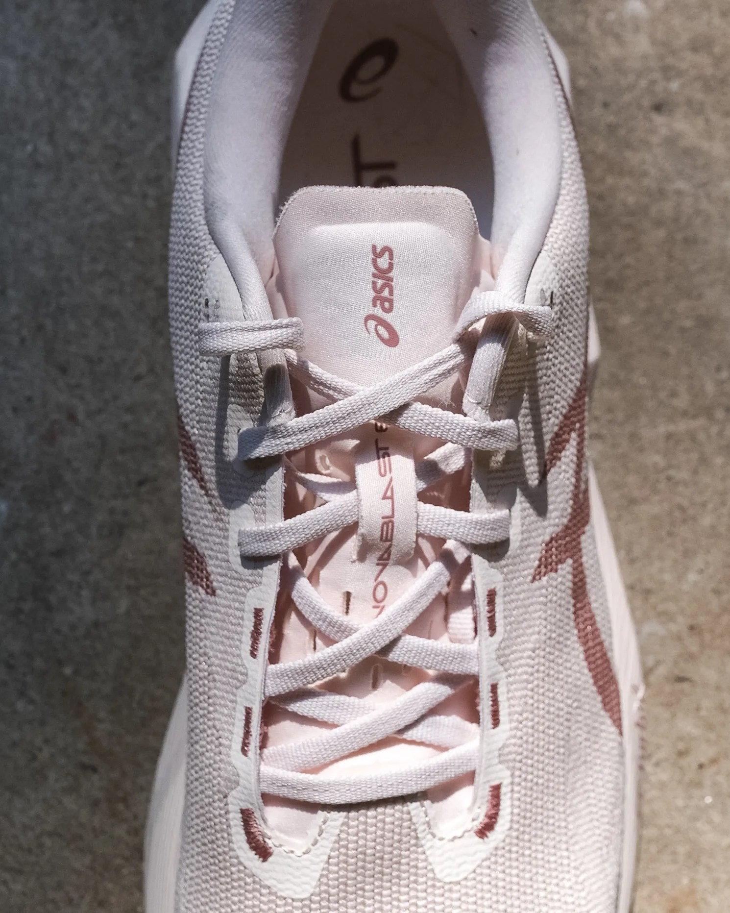 Close-up of a white and light pink Asics running shoe with laces tied in a standard crisscross pattern.