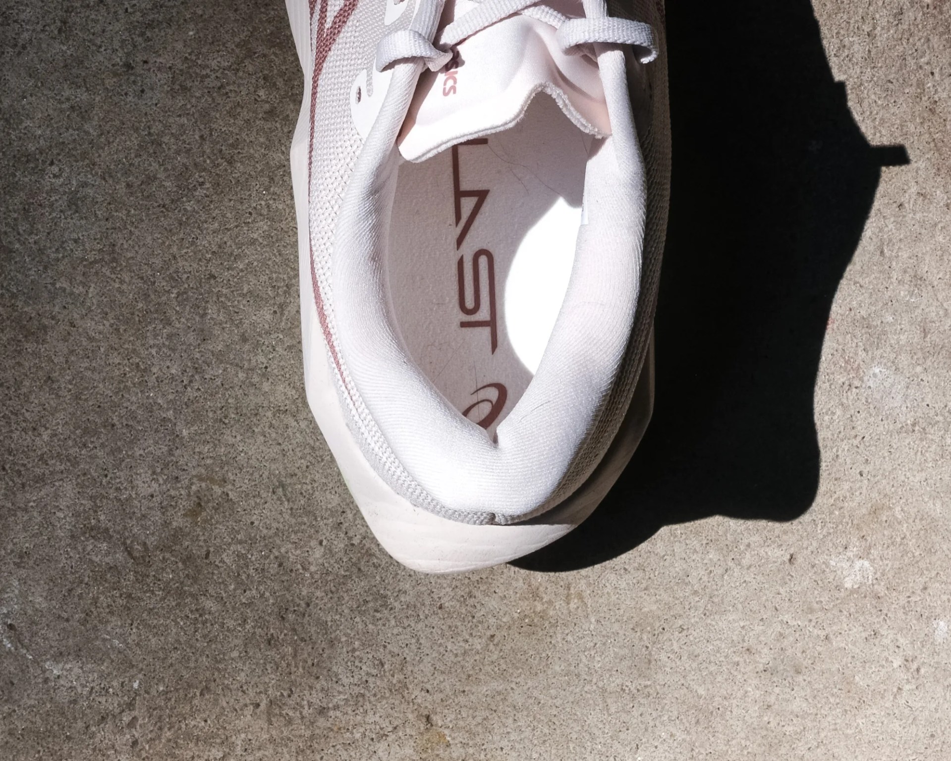 Top view of a white Asics running shoe on concrete ground.