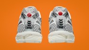 Pair of silver and white ASICS running shoes with red circular logos on the heels against an orange background.