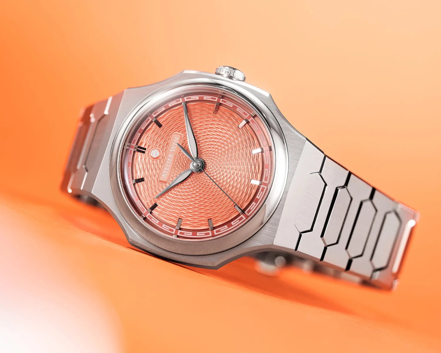 Silver metal wristwatch with an intricate orange textured dial and geometric bracelet links on an orange surface.