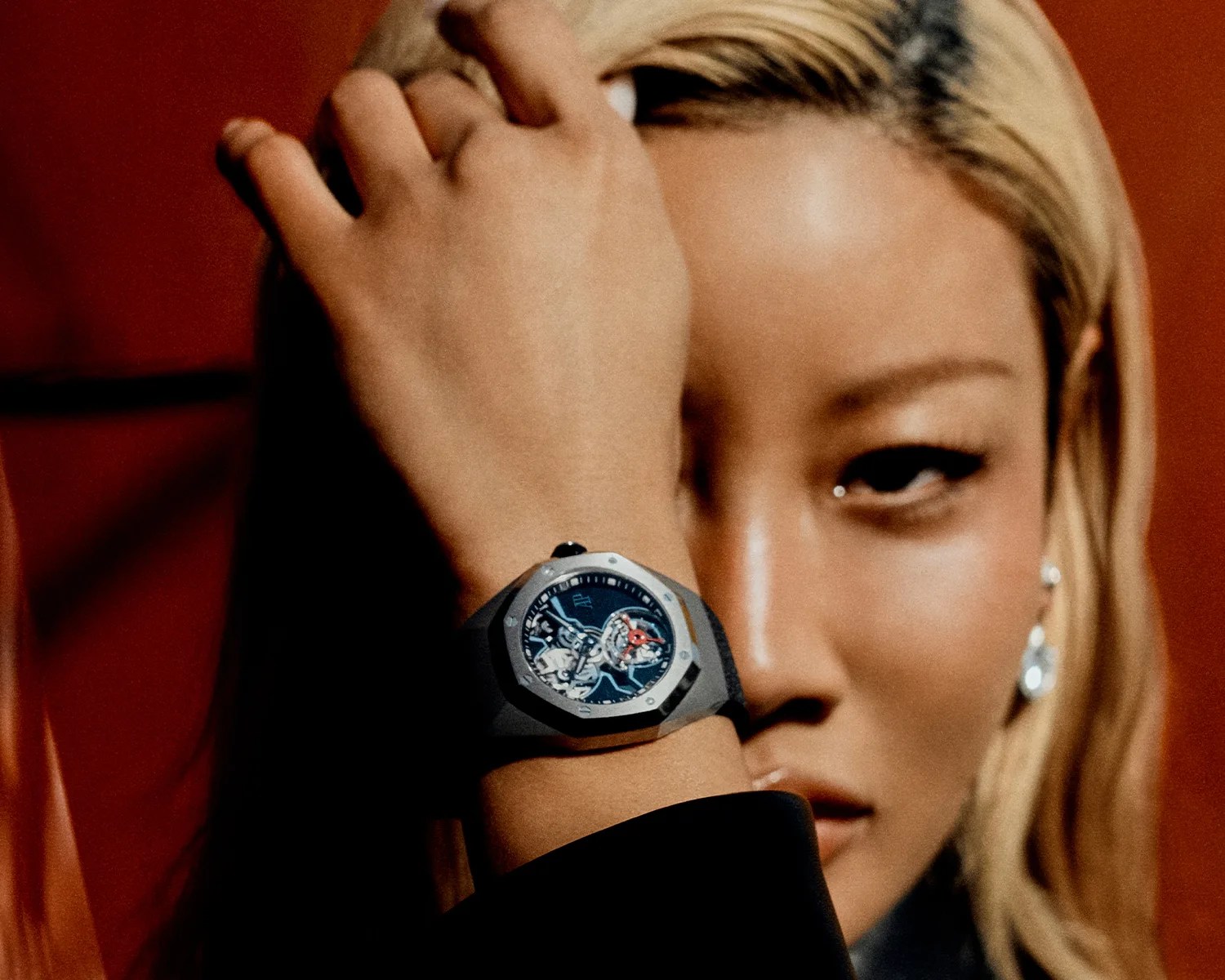 Black wristwatch with a silver octagonal bezel and visible mechanical movement worn on a wrist near a person's face.