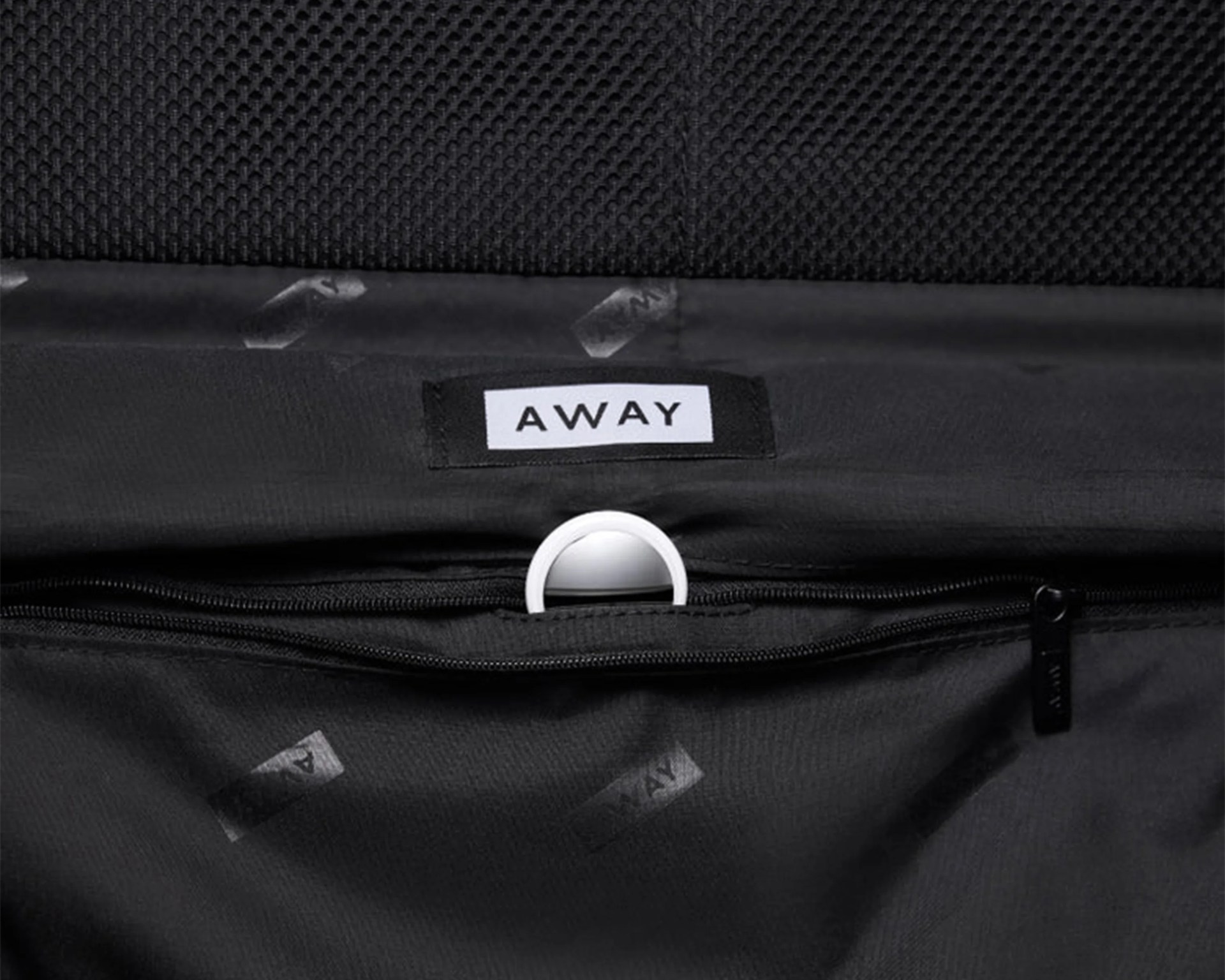 Black fabric interior of a bag with a white "AWAY" label and a white circular ring attached inside.
