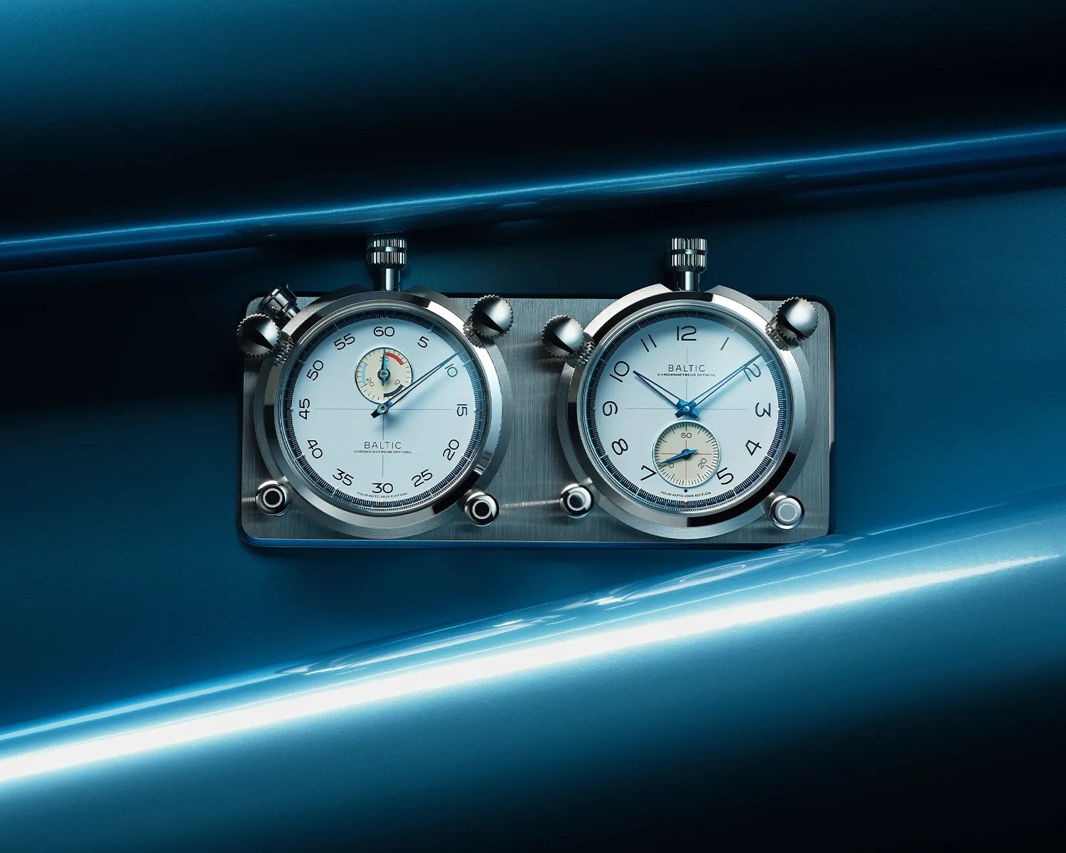 Dual silver Baltic chronograph timers with white dials mounted on a brushed metal plate against a blue background.