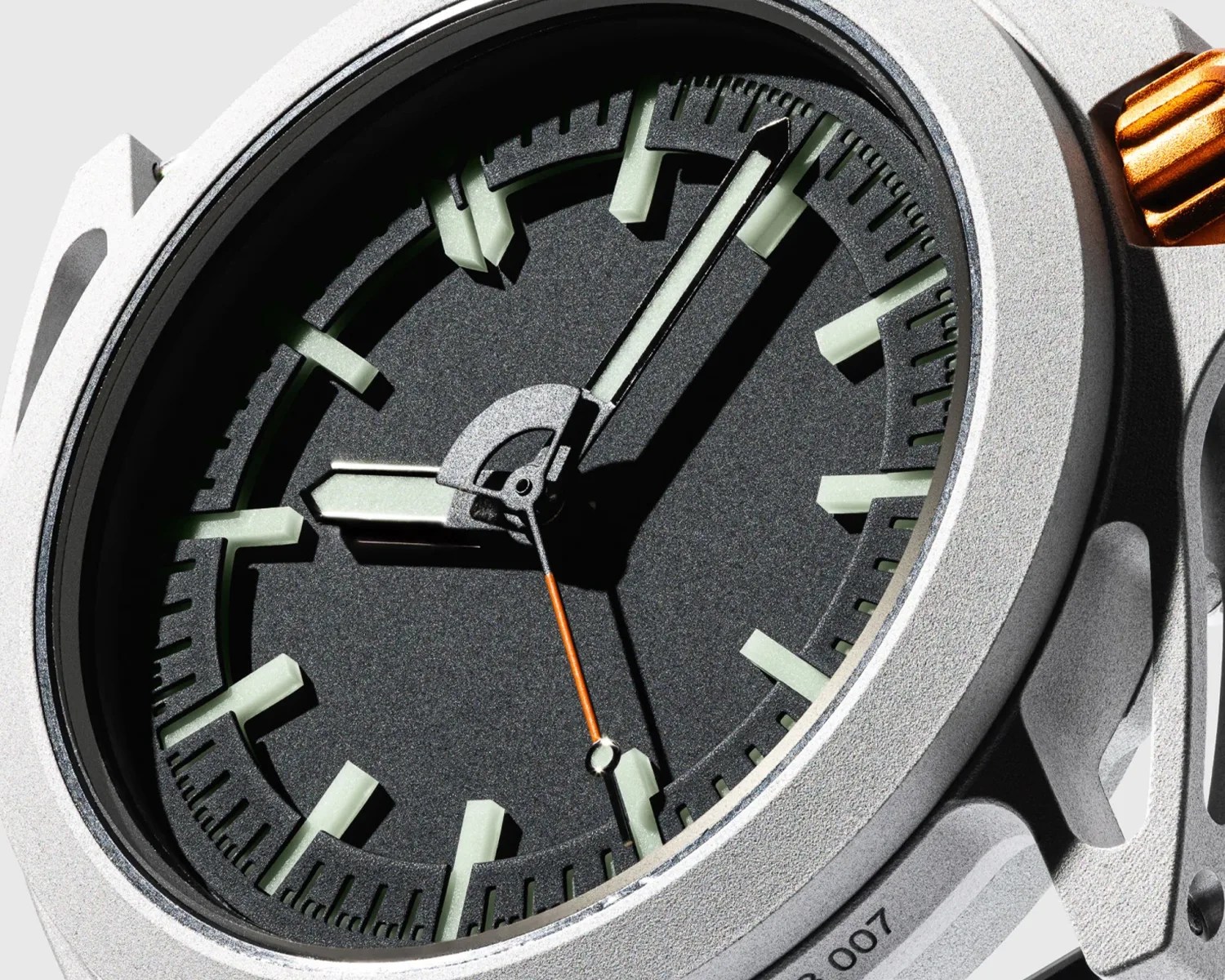 Close-up of a black watch dial with thick luminous hour markers and hands, housed in a textured silver case with an orange crown.