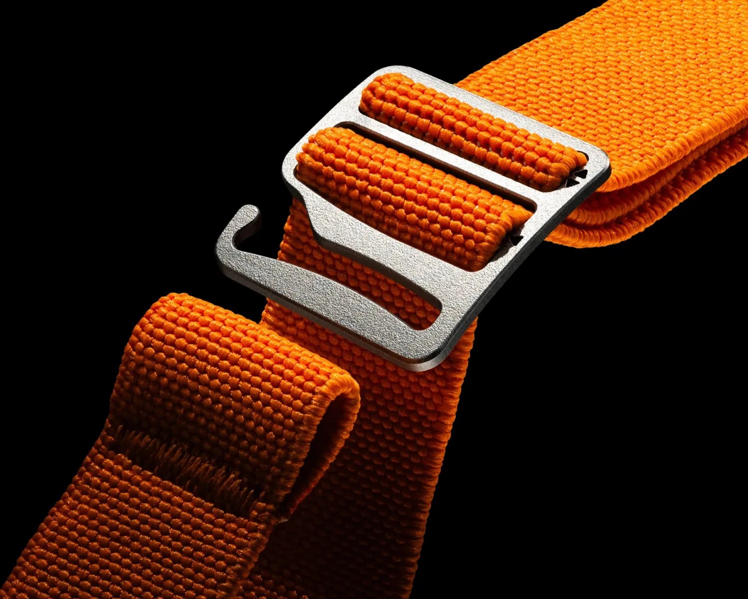 Close-up of an orange woven nylon strap with a silver metal hook buckle on a black background.