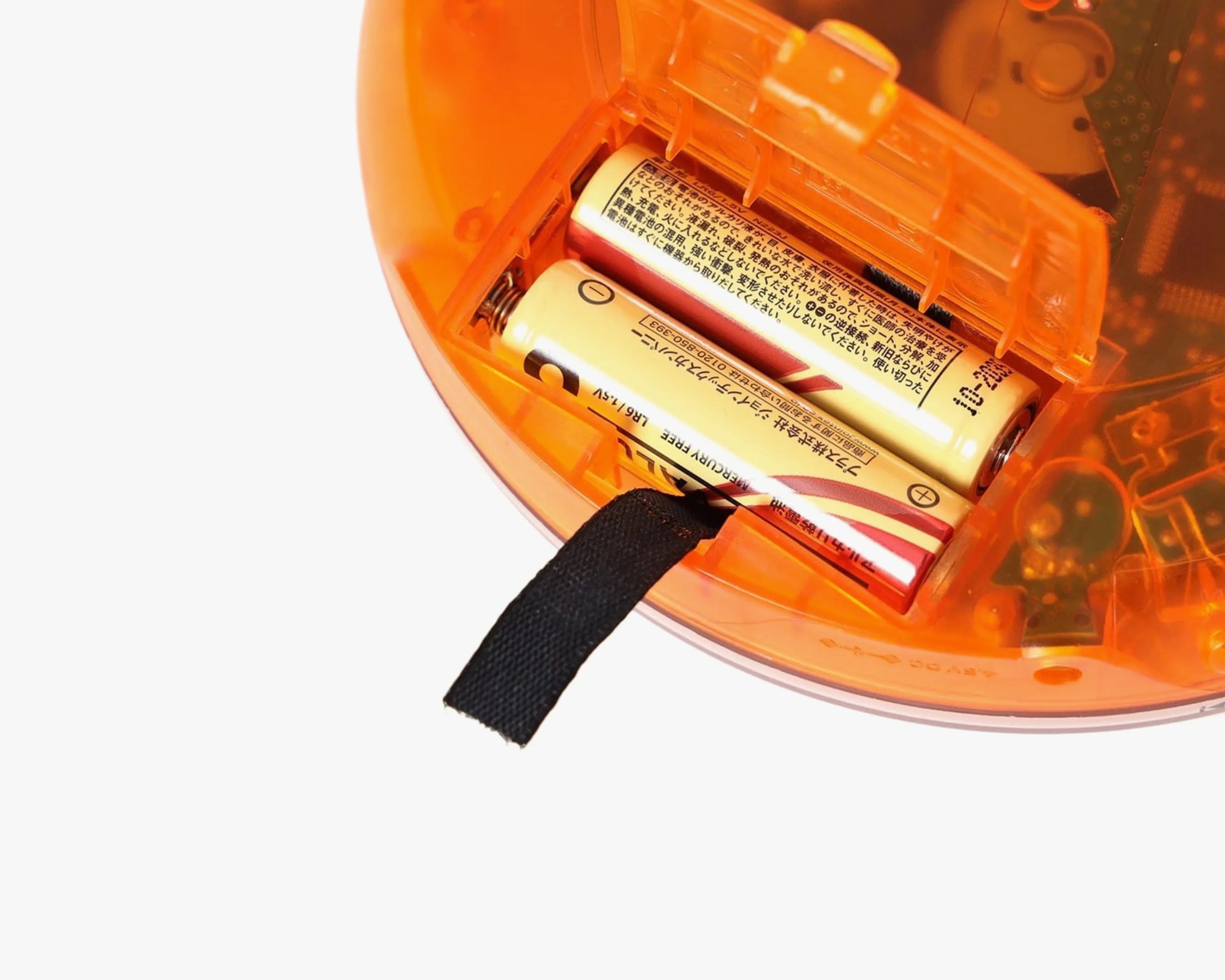 Two AA batteries with Japanese text inside an orange translucent plastic battery compartment with a black fabric pull tab.