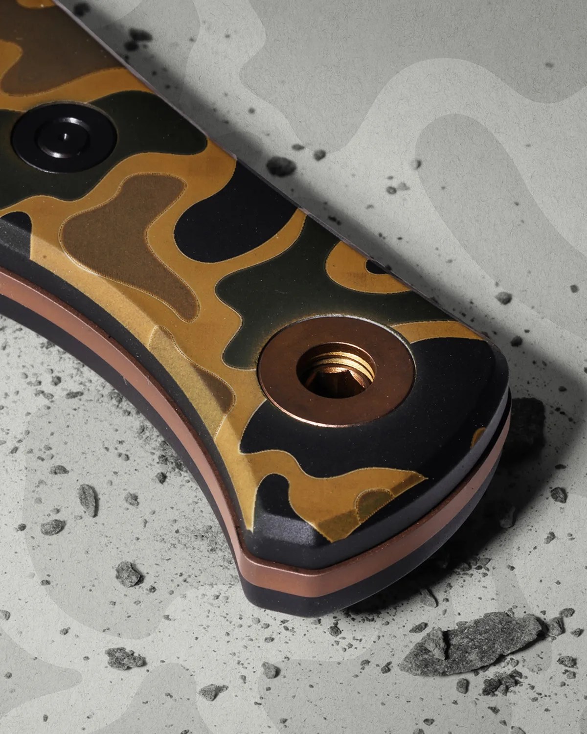 Close-up of a knife handle with a brown, black, and tan camouflage pattern and a copper-colored screw hole.
