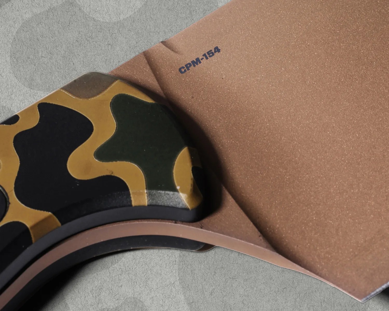 Close-up of a knife handle with green and brown camouflage pattern and a blade marked "CPM-154.