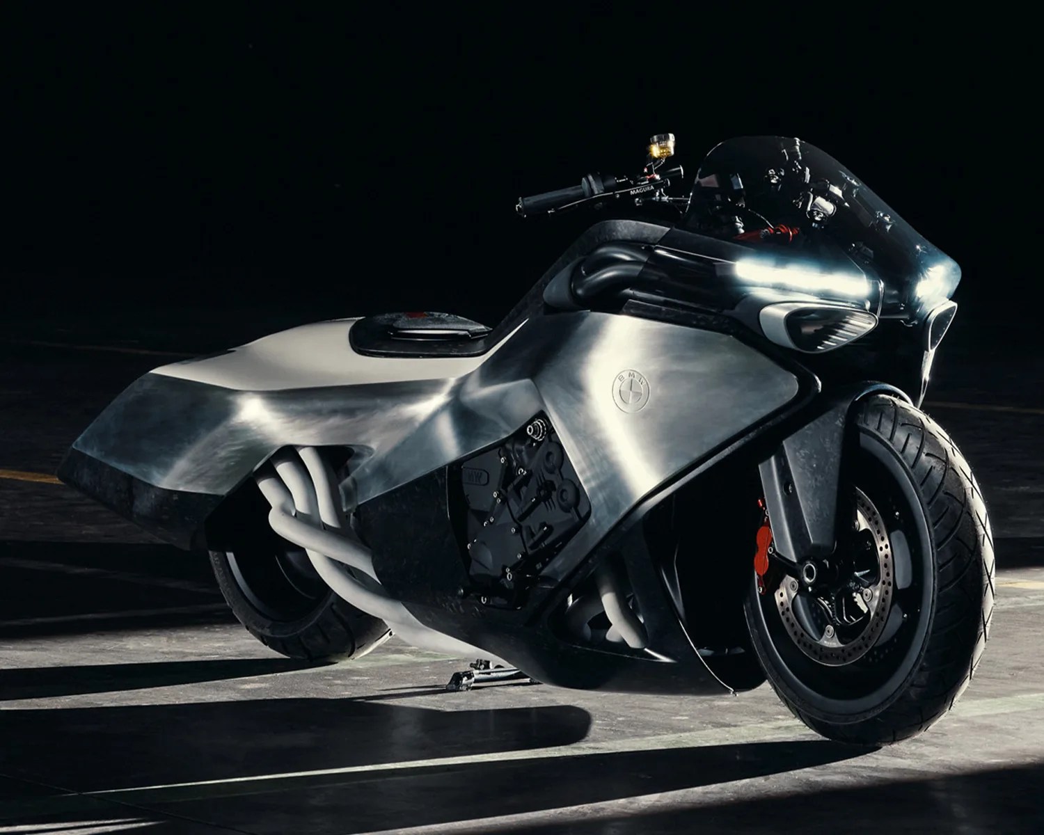 Sleek silver and black BMW motorcycle with aerodynamic fairing and exposed exhaust pipes on a dark floor.