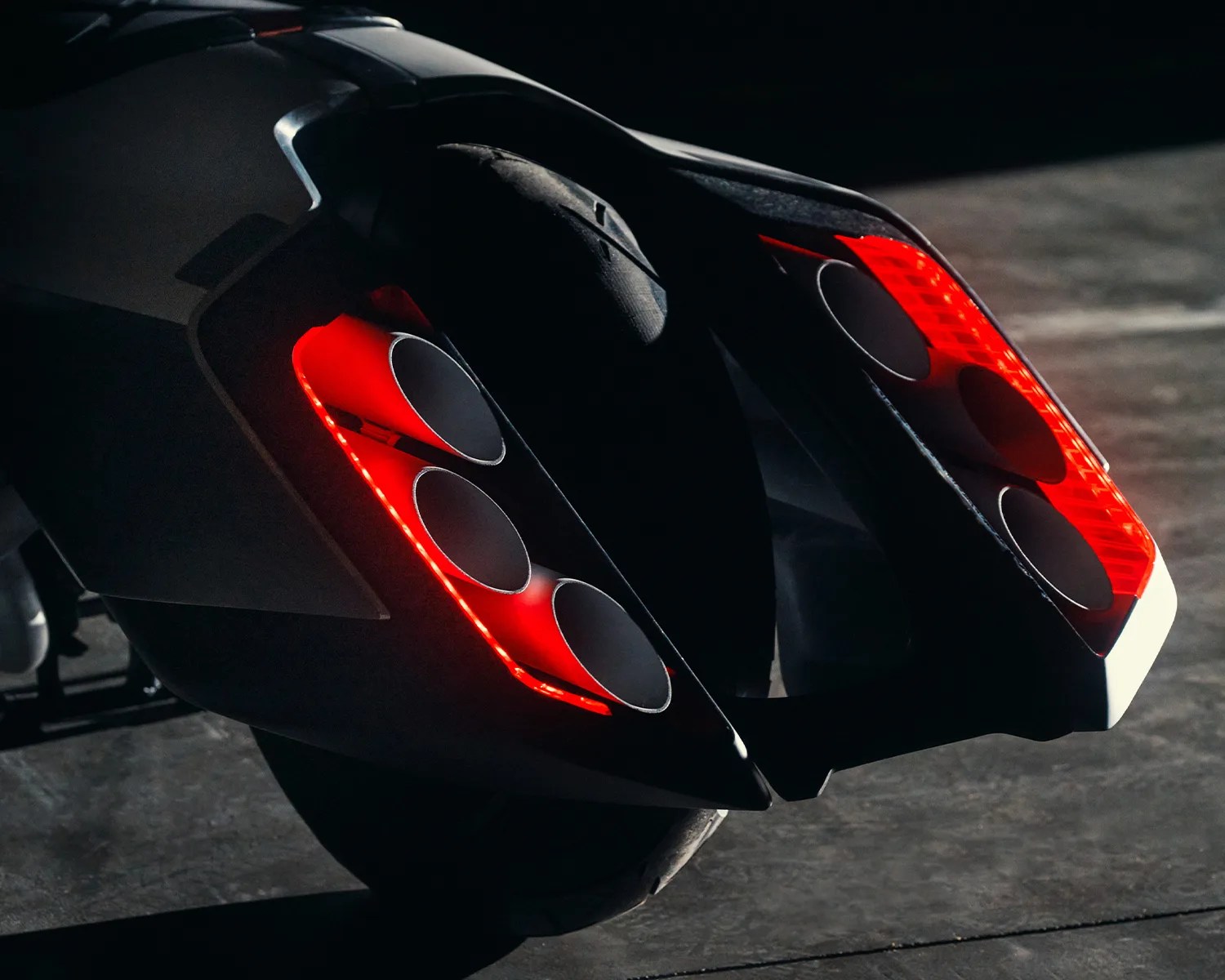 Rear view of a black motorcycle with six circular exhaust pipes and red LED tail lights.
