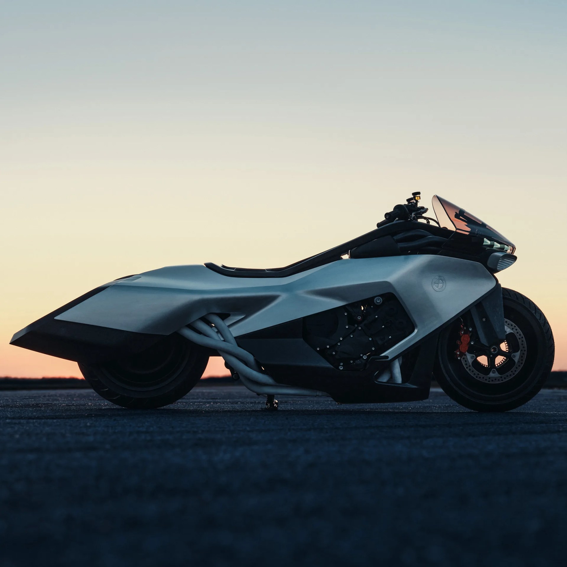 Silver and black futuristic BMW motorcycle with a sleek aerodynamic design parked on asphalt at sunset.