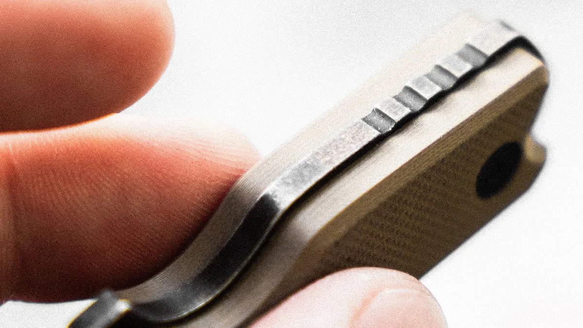 Close-up of a hand holding a tan textured object with a metal clip featuring ridges.