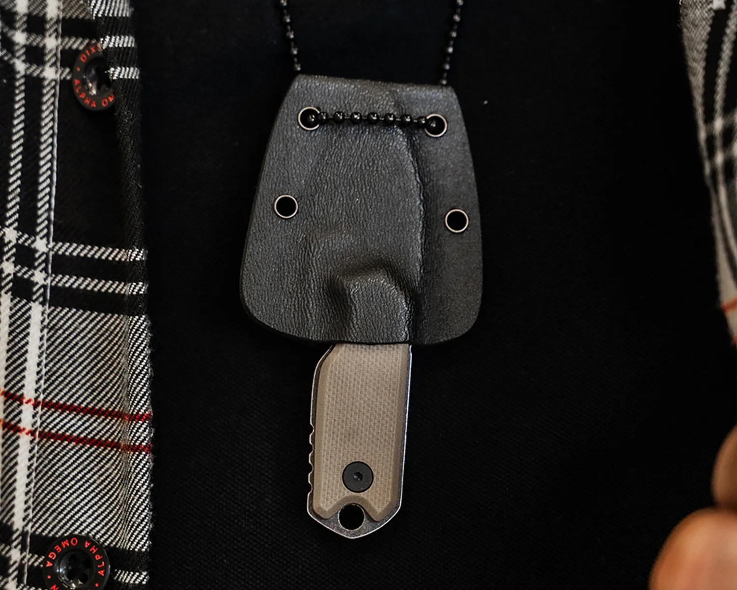 Small black leather sheath with metal rivets holding a compact knife with a textured handle.