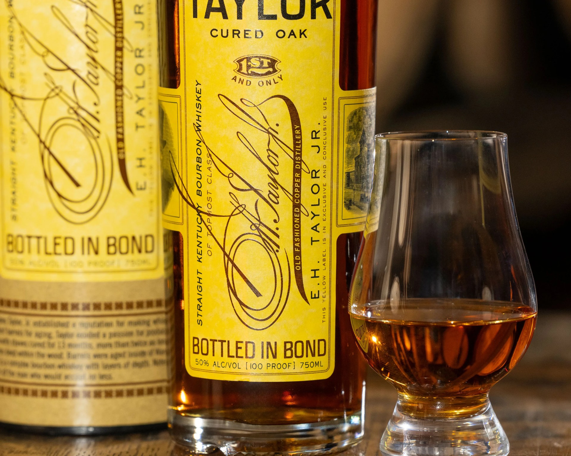 Close-up of a yellow-labeled bottle of E.H. Taylor bourbon whiskey next to a glass with amber whiskey.